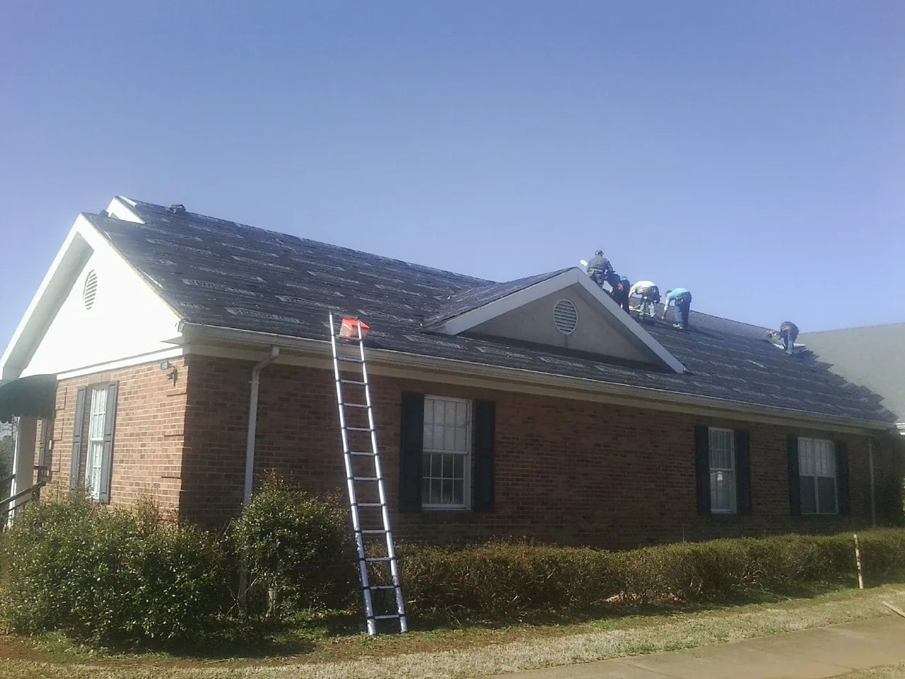 Crew tearing shingles off a brick ranch roof with a ladder set — Metal Roof Repair work by our crew in Ashton