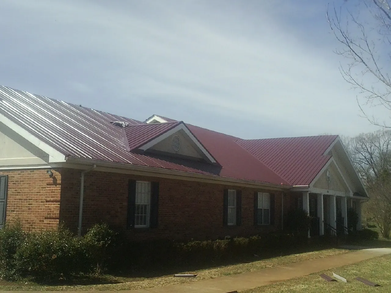 Red metal roof with gabled entries on a long brick building, from a Hail Damage Roof Repair job in Ashton