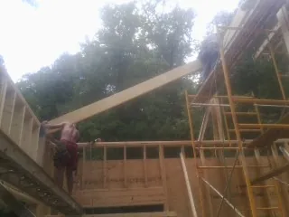 Carpenter raising a rafter beam on a new second story frame in Ashton