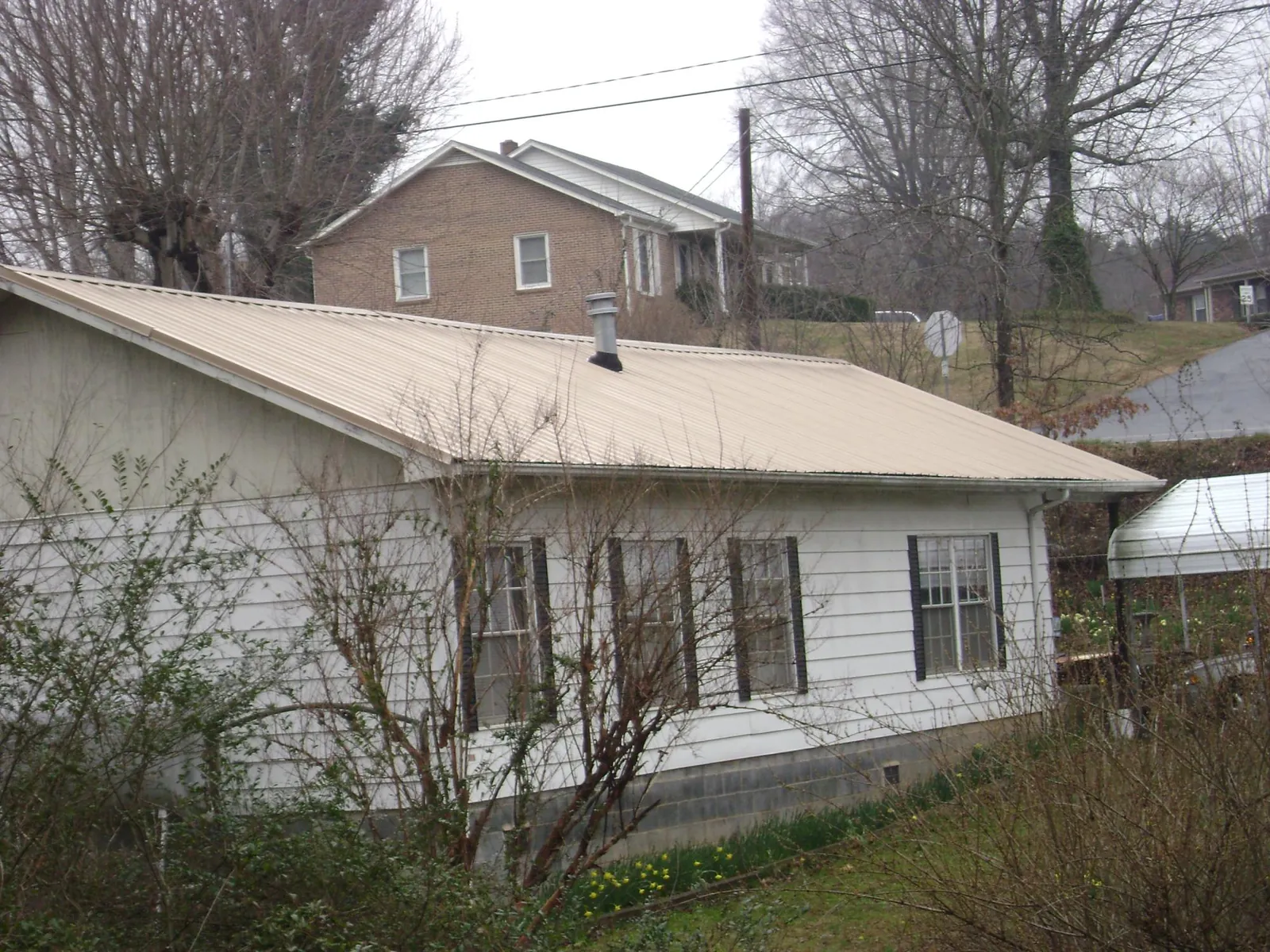 Tan metal roof on a white sided house set into a hillside — Commercial Roofing by Roofing Brothers in Ashton