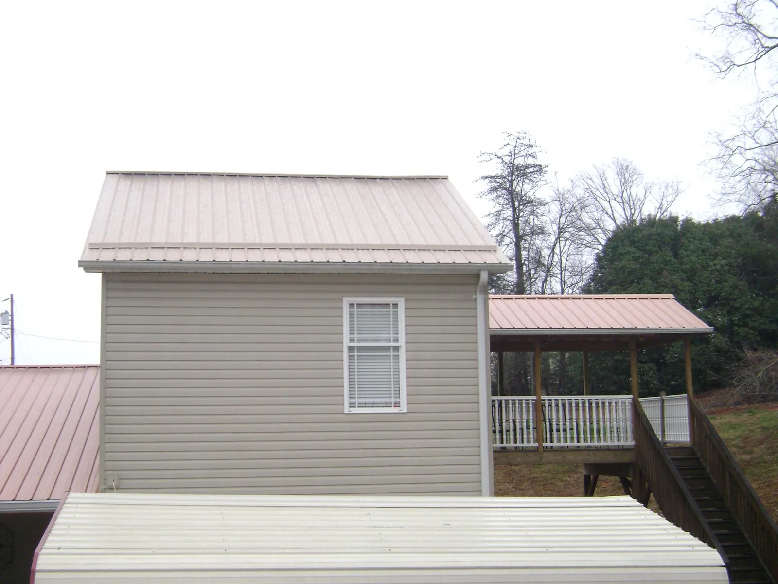 Tan metal roofs on a two story addition and attached porch, from a Roof Replacement job in Ashton